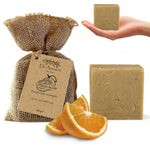 A bar of Dr. Ancient Citrus Soap body and hand soap shown with its burlap bag packaging, orange slices, and a hand holding another bar on a white background.