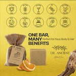 A bar of natural soap shown on a bright yellow background with promotional text and icons. The soap bar is light beige, next to orange slices and a burlap bag with a tag.