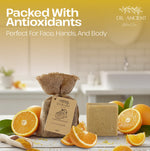A bar of natural soap next to a burlap bag of Dr. Ancient Hand & Body Soap, styled with fresh orange slices and a scoop of yellow powder on a white table, with a blurred kitchen background.