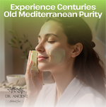 A woman in a white robe applies a pale green skincare cream from a small bottle to her cheek. Large text at the top reads 'Experience Centuries Old Mediterranean Purity' and the bottom-left corner shows the brand 'DR.