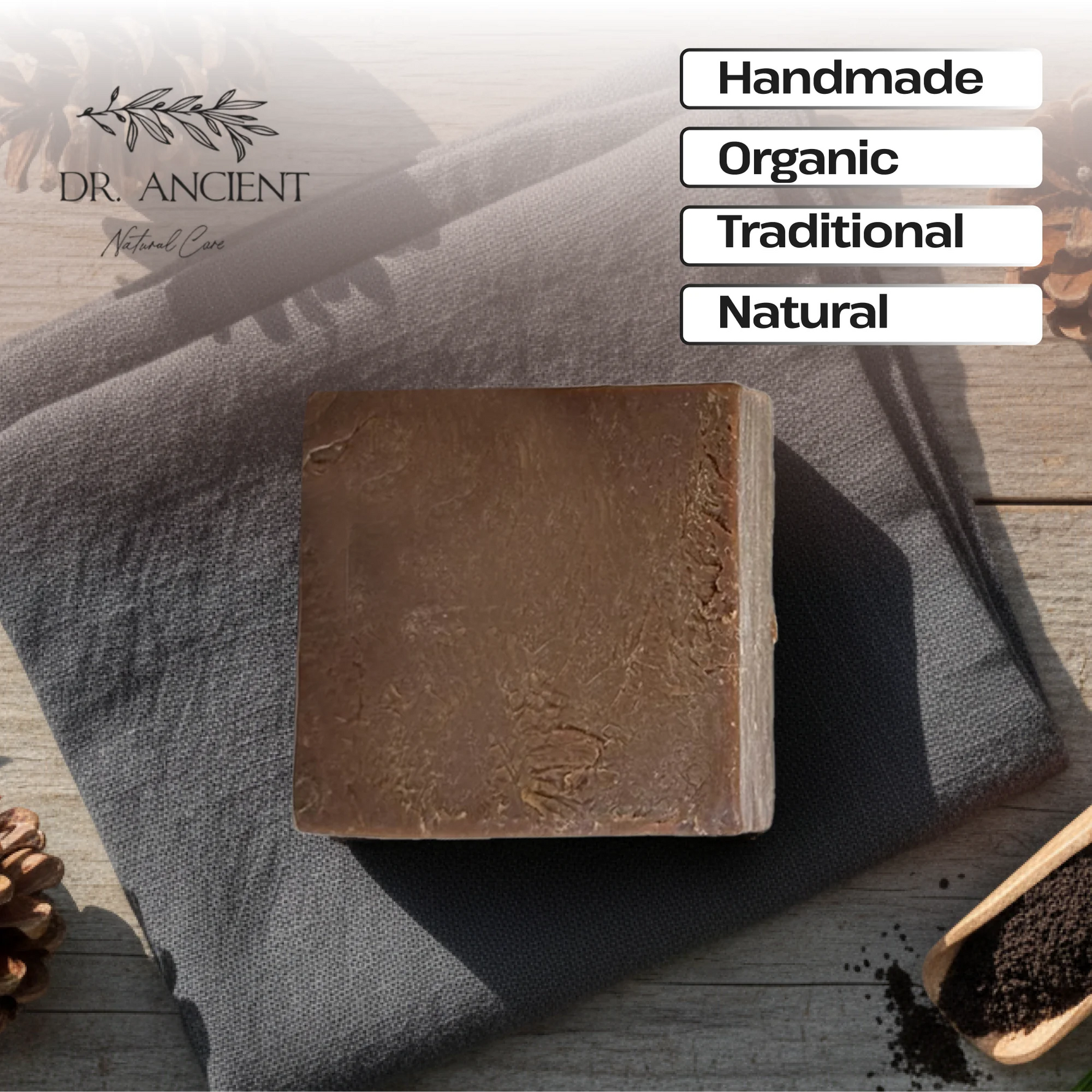 A rectangular bar of brown soap rests on a dark gray cloth over a rustic wooden surface, with pinecones and a small wooden scoop of dark powder nearby. White text boxes on the right read 'Handmade', 'Organic', 'Traditional', and 'Natural', and the brand name 'DR.