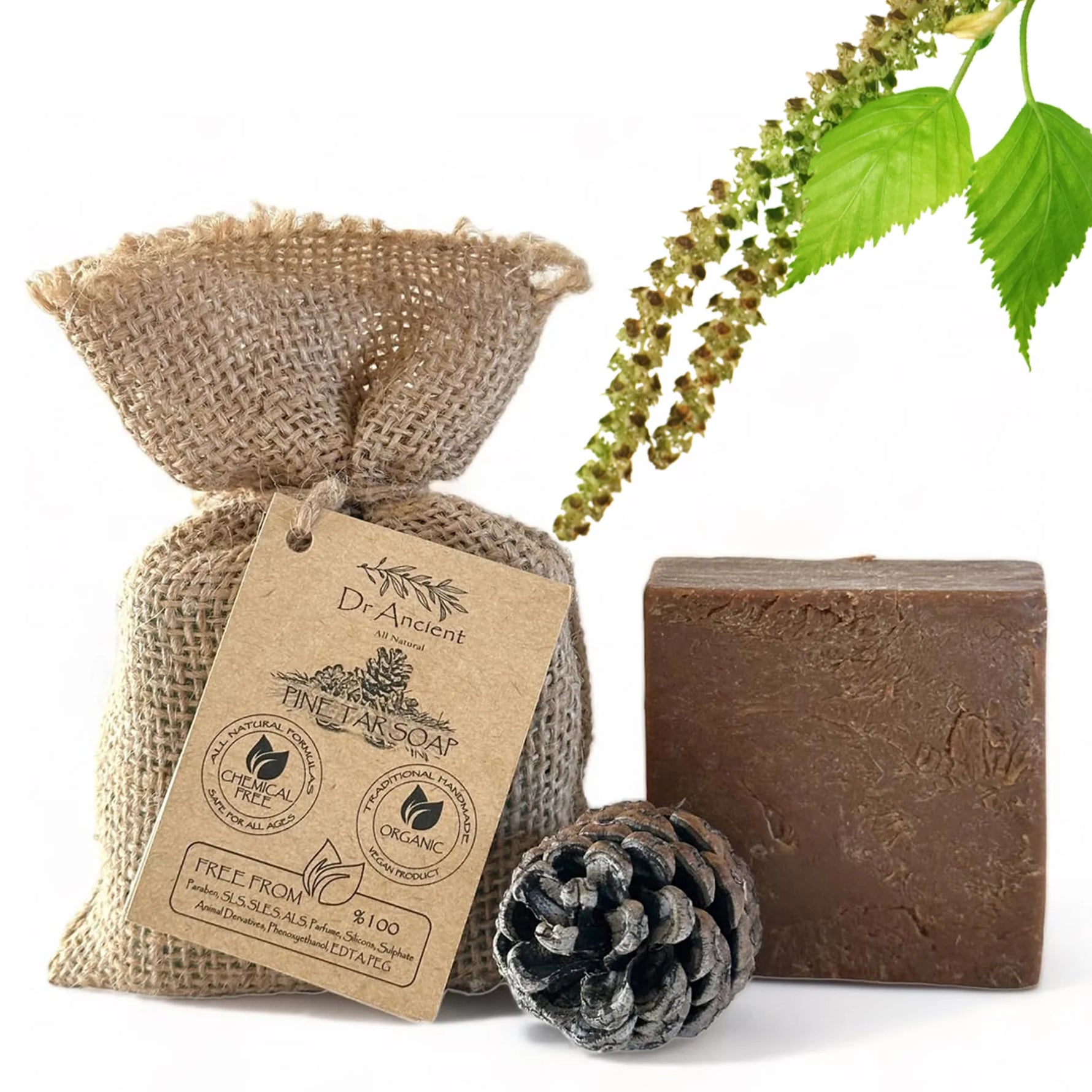 A bar of Dr. Ancient Pine Tar Soap in a rustic brown color, displayed next to its burlap packaging bag with a kraft paper tag, a pinecone, and green birch leaves on a white background.