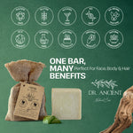 A bar of natural soap displayed with a burlap bag tag and green leaves on a dark green background, surrounded by certification-style icons and the brand name Dr. Ancient Natural Care.