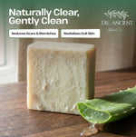Aloe Vera Soap Bar by Dr. Ancient Natural Care, shown as a rectangular pale green soap bar next to a burlap drawstring bag with a branded paper tag, on a dark green background with promotional text.