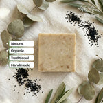 Handmade soap bar on a textured surface with leaves and seeds, labeled as natural, organic, traditional, and handmade.