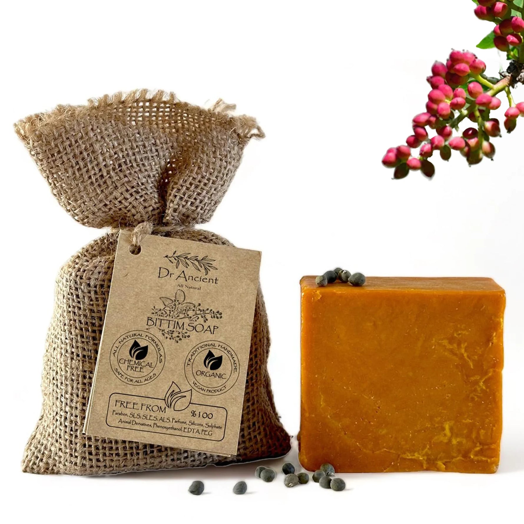 A bar of orange-yellow herbal skin soap next to a burlap pouch with a paper tag reading Dr. Aumont BYLINE SOAP, with small dark berries scattered on a white background and pink flowers in the corner.