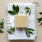 Block of soap on a white towel with green leaves, labeled as natural, organic, traditional, and handmade by Dr. Ancient.
