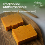 Two rectangular bars of handmade orange soap with small dark specks, resting on a round wooden board. The image features promotional text overlays reading 'Traditional Craftsmanship', 'No Parabens Or Silicons', and 'No Palm Oil, Perfumes, Or Dyes', along with the 'DR.